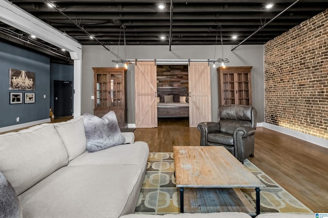 living room with a towering ceiling, brick wall, a barn door, and hardwood / wood-style floors