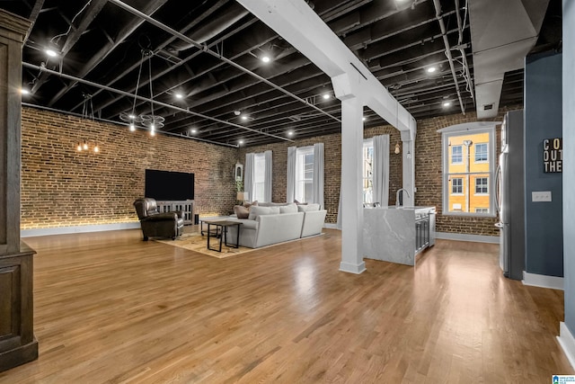 unfurnished living room featuring brick wall, wood-type flooring, and sink