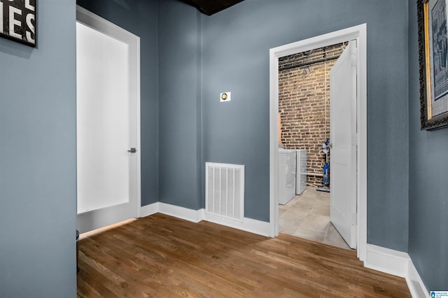 spare room featuring separate washer and dryer, brick wall, and wood-type flooring