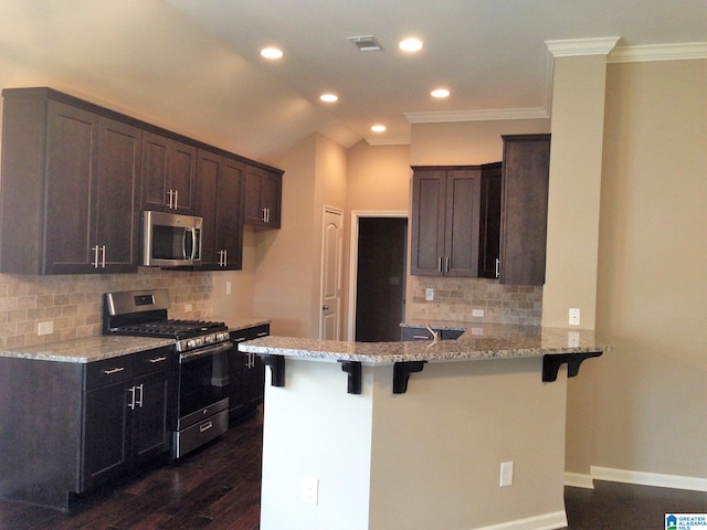 kitchen featuring light stone counters, kitchen peninsula, a kitchen bar, appliances with stainless steel finishes, and ornamental molding