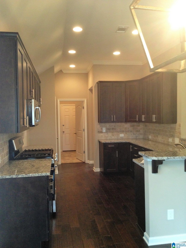 kitchen with appliances with stainless steel finishes, dark hardwood / wood-style flooring, a breakfast bar, light stone counters, and backsplash