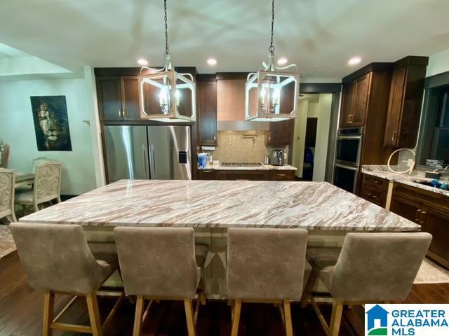 kitchen featuring hardwood / wood-style flooring, hanging light fixtures, a center island, a kitchen bar, and appliances with stainless steel finishes