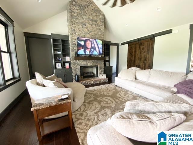 living room featuring built in shelves, vaulted ceiling, dark hardwood / wood-style flooring, and a stone fireplace