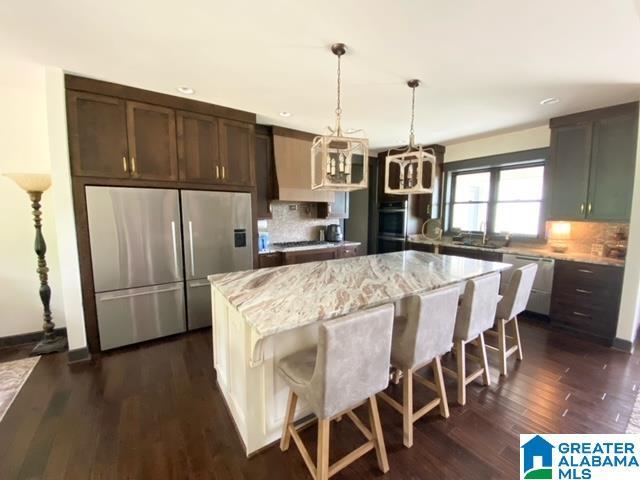 kitchen with stainless steel appliances, tasteful backsplash, light stone countertops, a kitchen island, and dark wood-type flooring