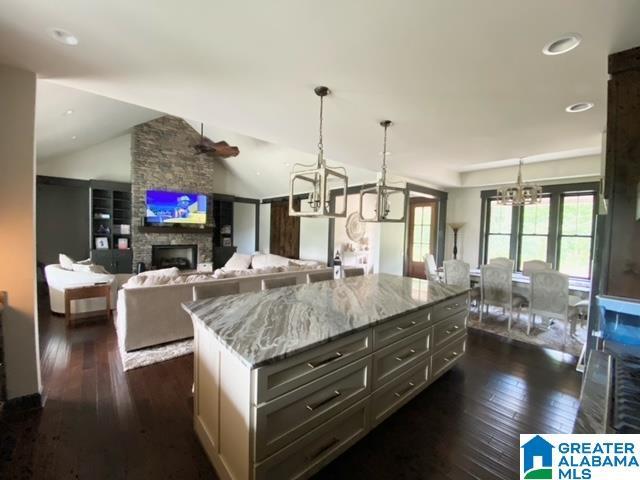 kitchen with a stone fireplace, a center island, hanging light fixtures, and light stone countertops