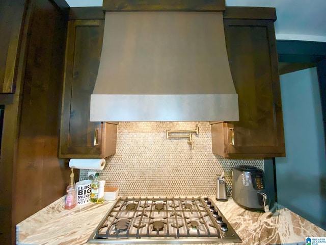 kitchen with gas stovetop, backsplash, light stone counters, and wall chimney exhaust hood