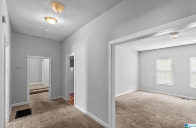 hall featuring light colored carpet and a textured ceiling