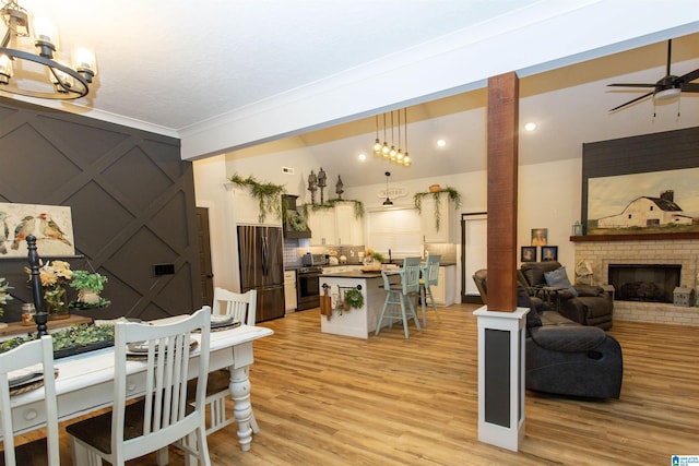 dining area with light hardwood / wood-style floors, vaulted ceiling, ceiling fan, and a fireplace