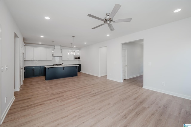 kitchen featuring open floor plan, premium range hood, stainless steel microwave, backsplash, and light wood-style flooring