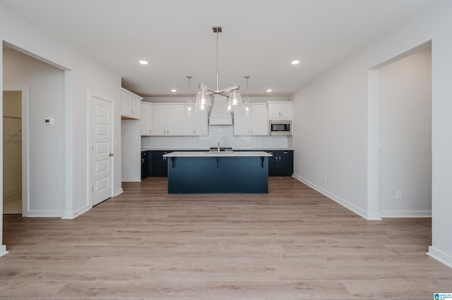 kitchen with light wood-style flooring, stainless steel microwave, white cabinetry, a sink, and backsplash