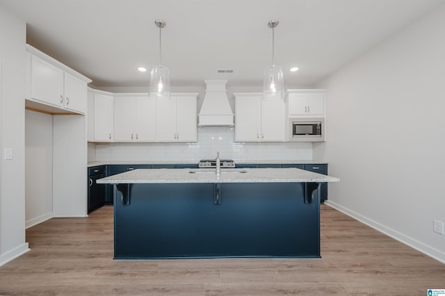 kitchen with white cabinets, tasteful backsplash, custom exhaust hood, and stainless steel microwave