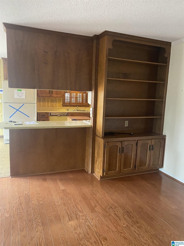 kitchen featuring a sink, light countertops, a textured ceiling, a peninsula, and wood finished floors
