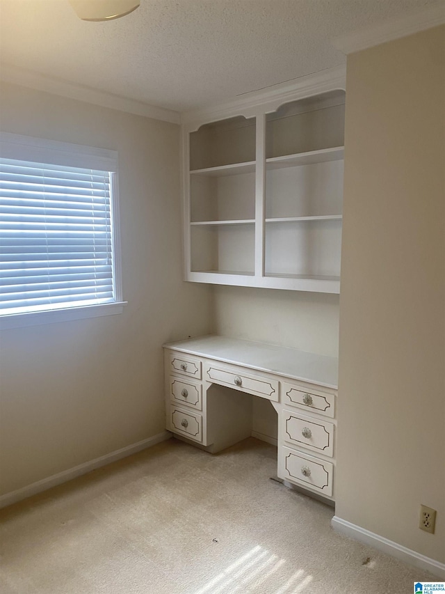 unfurnished office featuring crown molding, light carpet, built in desk, a textured ceiling, and baseboards