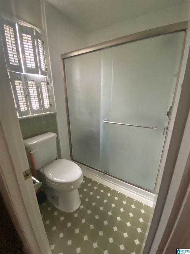 bathroom featuring toilet, tile patterned floors, and a shower stall