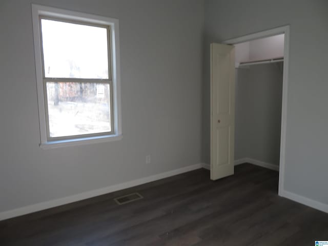 unfurnished bedroom featuring dark wood-type flooring, a closet, and multiple windows