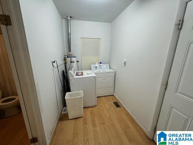 clothes washing area with washer and clothes dryer and light wood-type flooring