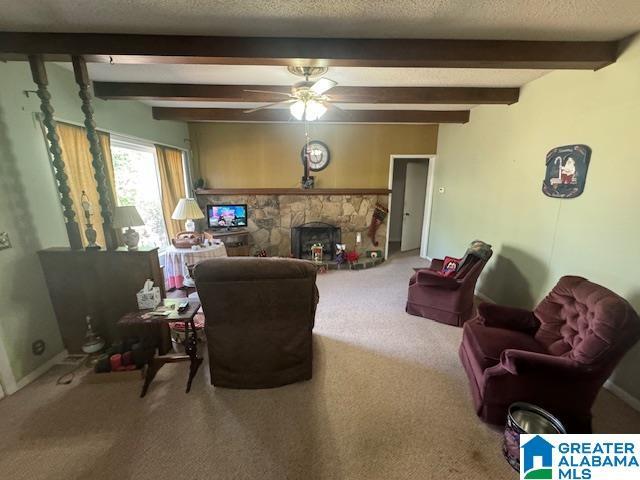 living room with a fireplace, ceiling fan, beamed ceiling, and carpet floors