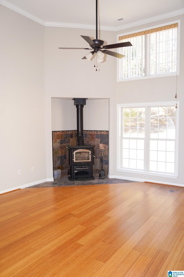 unfurnished living room featuring ceiling fan, wood-type flooring, a wood stove, and ornamental molding