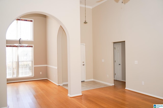 unfurnished room with ceiling fan, ornamental molding, light hardwood / wood-style floors, and a high ceiling