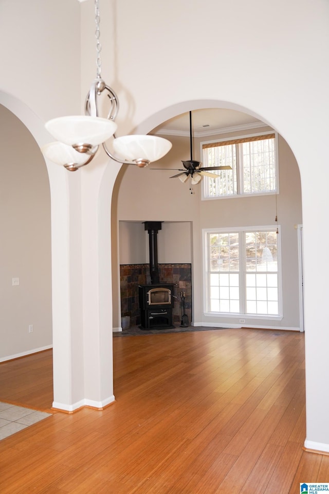 unfurnished living room featuring ceiling fan, ornamental molding, a wood stove, and hardwood / wood-style floors