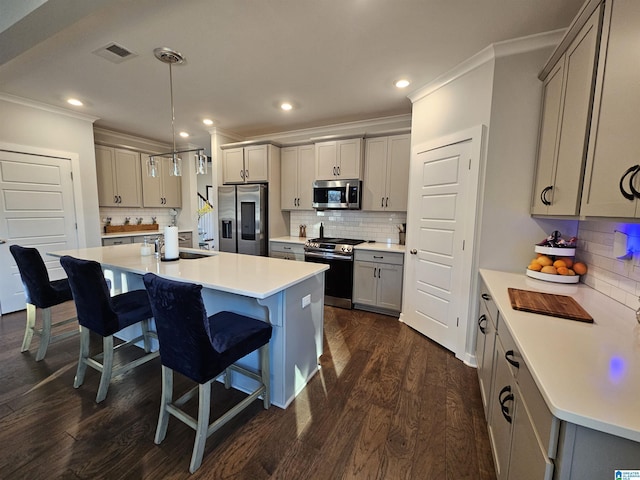 kitchen with a center island with sink, gray cabinetry, stainless steel appliances, pendant lighting, and tasteful backsplash