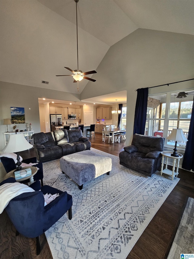 living room featuring dark wood-type flooring, plenty of natural light, high vaulted ceiling, and ceiling fan with notable chandelier