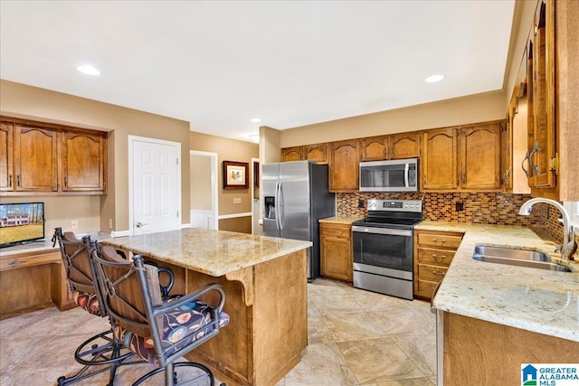 kitchen with stainless steel appliances, sink, light stone counters, a breakfast bar area, and decorative backsplash