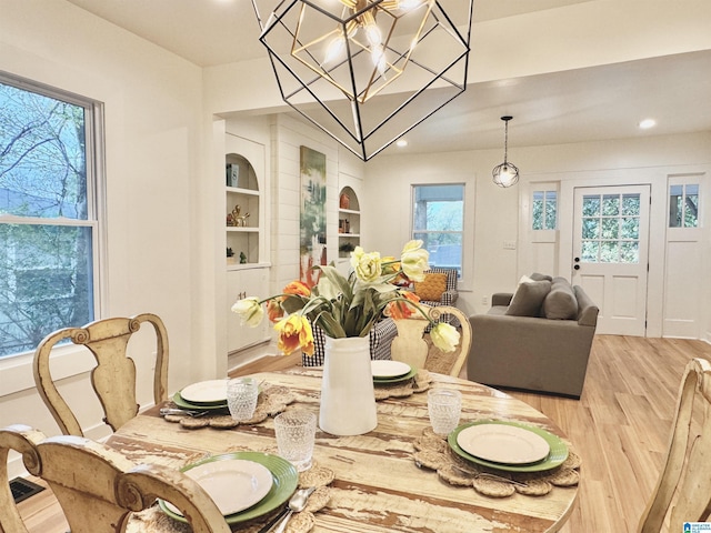 dining space featuring light hardwood / wood-style floors, a notable chandelier, and built in features