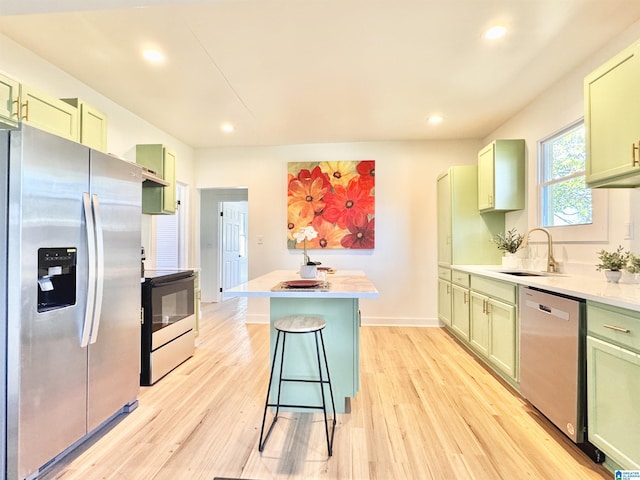 kitchen featuring stainless steel appliances, sink, green cabinets, a kitchen breakfast bar, and light hardwood / wood-style flooring