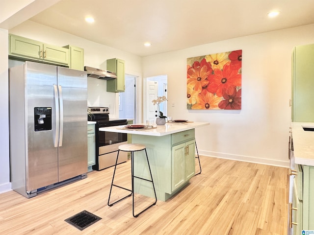 kitchen featuring stainless steel appliances, green cabinets, light wood-type flooring, a breakfast bar area, and a kitchen island