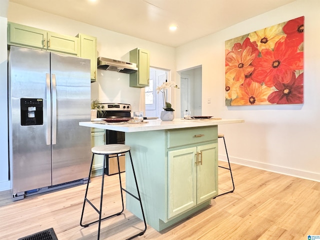 kitchen featuring a breakfast bar, light wood-type flooring, stainless steel fridge, and green cabinetry