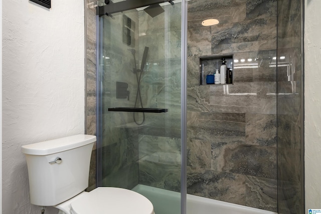 bathroom featuring a shower with door and toilet