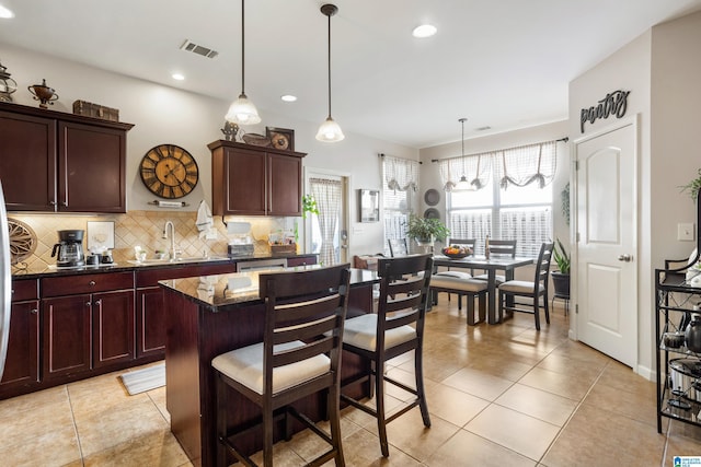 kitchen featuring a center island, decorative light fixtures, decorative backsplash, dark stone counters, and sink