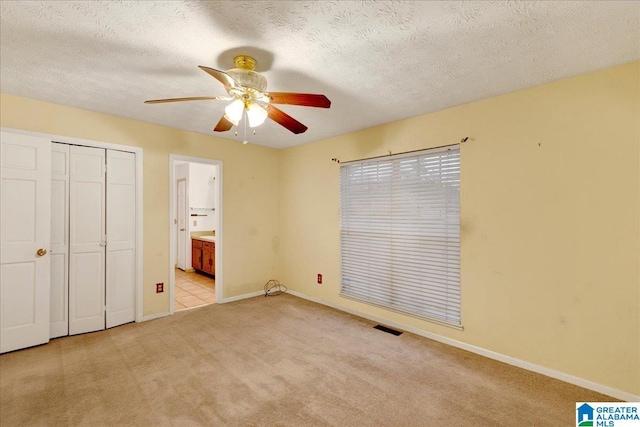 unfurnished bedroom with ensuite bathroom, light colored carpet, ceiling fan, and a textured ceiling