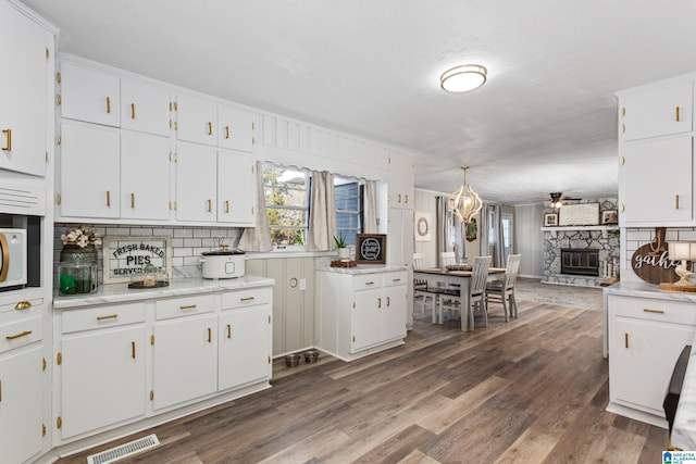 kitchen featuring ceiling fan, dark hardwood / wood-style flooring, decorative backsplash, a fireplace, and white cabinetry