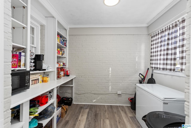 laundry area featuring crown molding, brick wall, hardwood / wood-style flooring, and a wealth of natural light