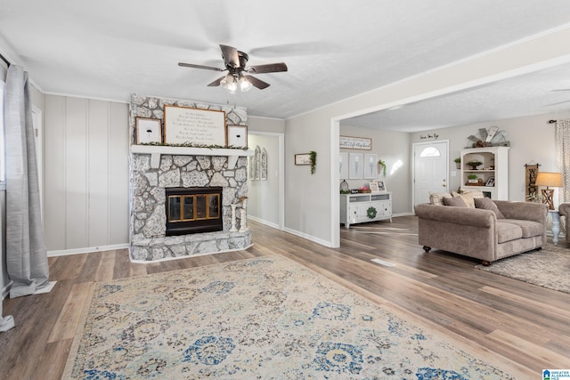 living room with ceiling fan, wood-type flooring, and a stone fireplace