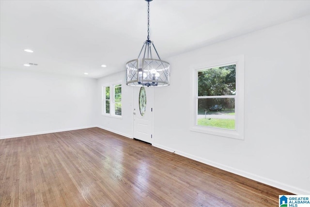 empty room featuring wood-type flooring and an inviting chandelier