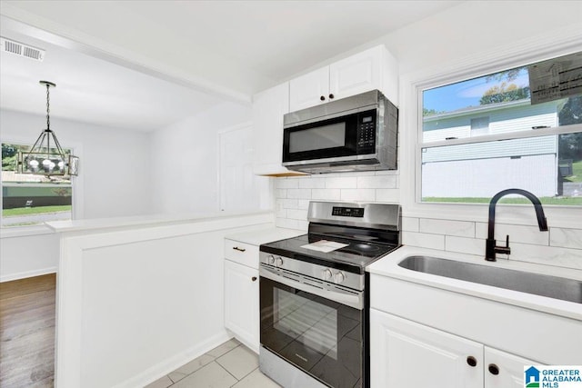 kitchen with stainless steel appliances, sink, white cabinetry, decorative backsplash, and a chandelier