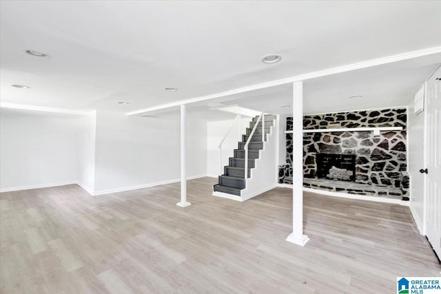 basement with light hardwood / wood-style flooring and a stone fireplace