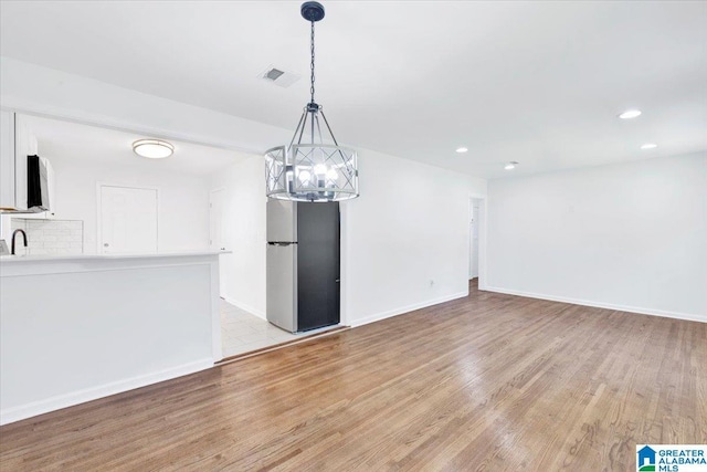 unfurnished dining area featuring an inviting chandelier, light wood-type flooring, and sink