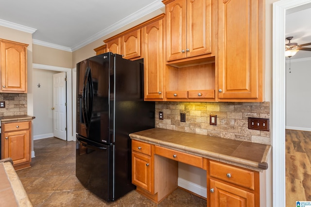 kitchen featuring ceiling fan, tile counters, black fridge, ornamental molding, and built in desk