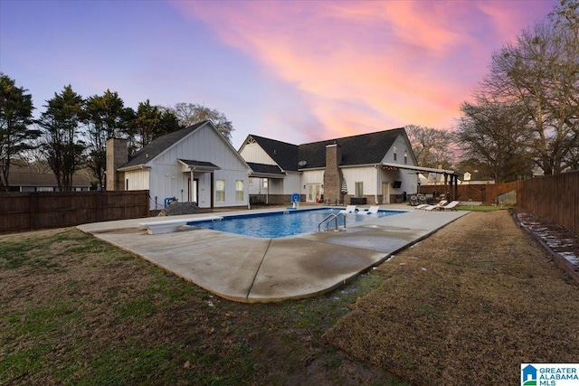 pool at dusk with a diving board, a patio, and a lawn