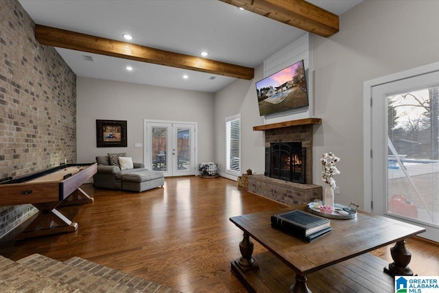 living room with beam ceiling, a brick fireplace, a wealth of natural light, and hardwood / wood-style flooring