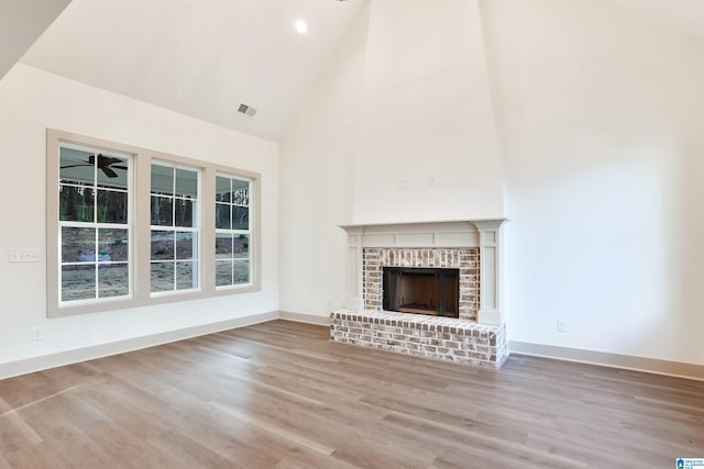 unfurnished living room featuring ceiling fan, light wood-type flooring, a brick fireplace, and high vaulted ceiling