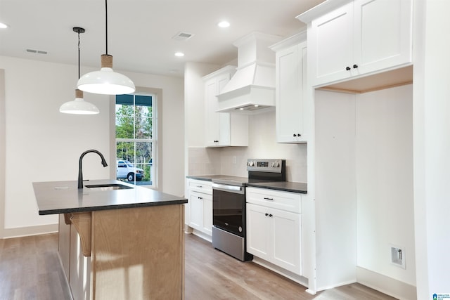 kitchen with sink, a kitchen island with sink, premium range hood, electric stove, and pendant lighting