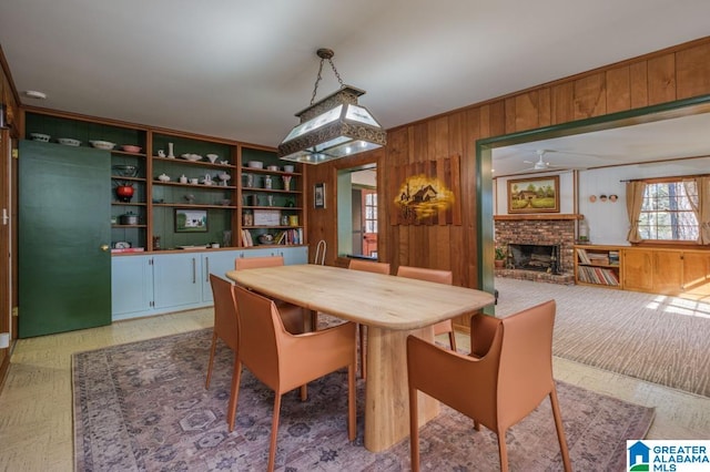 dining area with a fireplace, ceiling fan, and wooden walls