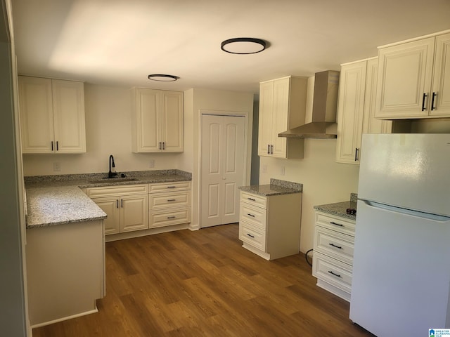 kitchen featuring white cabinets, white refrigerator, dark wood-type flooring, sink, and wall chimney range hood