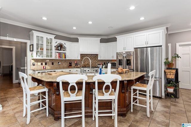 kitchen featuring appliances with stainless steel finishes, a large island with sink, a breakfast bar, decorative backsplash, and white cabinetry