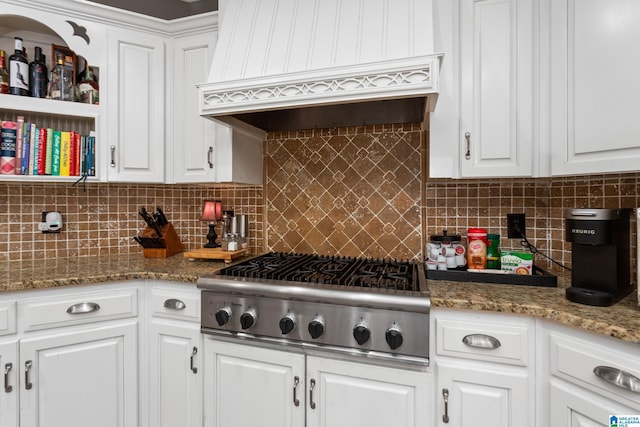 kitchen with custom range hood, stainless steel gas stovetop, light stone counters, decorative backsplash, and white cabinetry